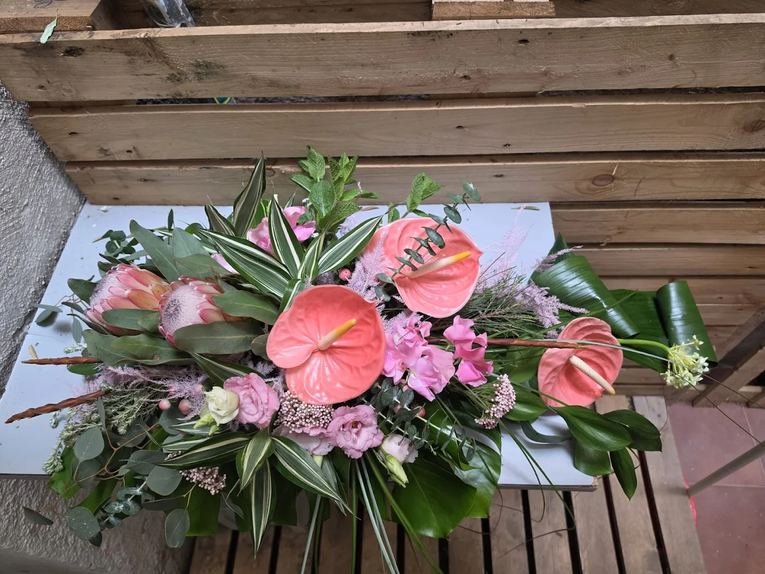 Centro alargado de anturios rosas y protea decorando una terraza de madera en Madrid